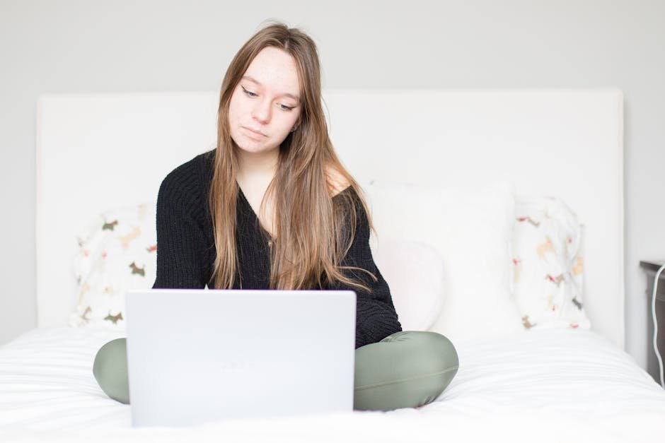 Young woman focused on her laptop while sitting in a cozy bedroom. Modern lifestyle concept.