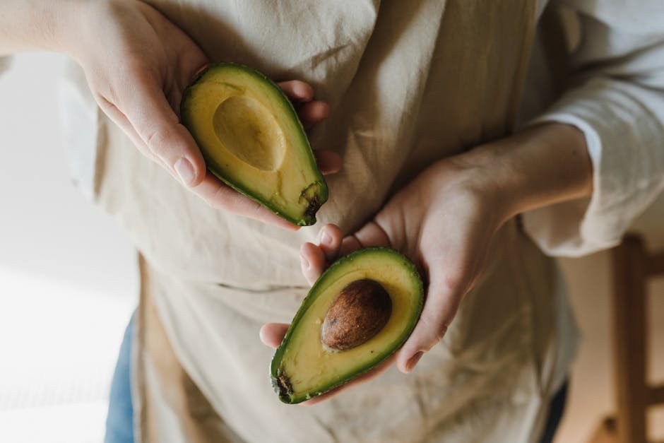Close-up of hands holding a ripe avocado sliced in half, showcasing its vibrant green flesh.