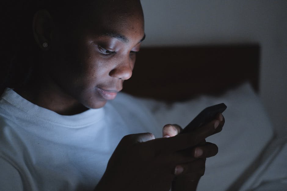 Young woman using a smartphone in a dimly lit room, focusing intently on the screen.