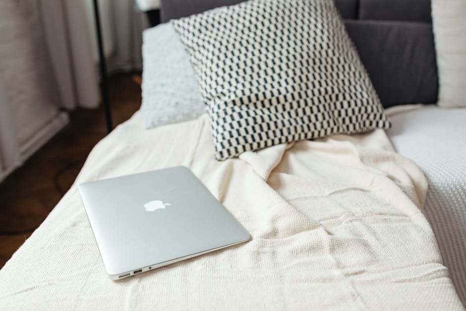 A minimalist scene of a laptop on a textured bed with pillows, capturing a relaxed and modern atmosphere.