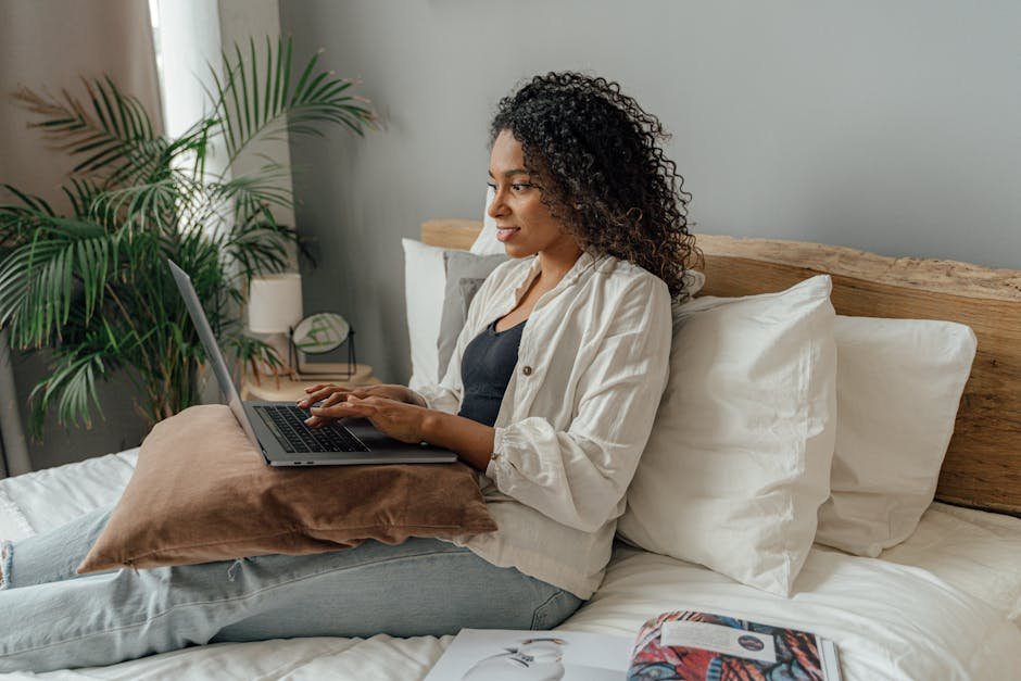 A relaxed woman using a laptop in a cozy bedroom while working remotely. Ideal for home office and lifestyle concepts.