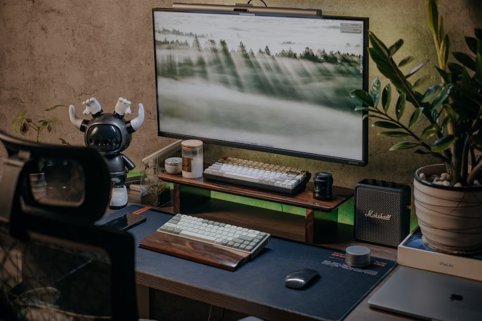 Stylish home office desk with gadgets, plant, and computer screen displaying nature wallpaper.