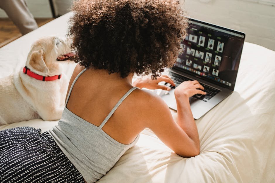 A woman using a laptop while relaxing with her dog on a cozy bed.