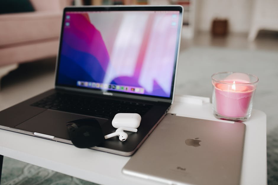 Cozy setup with a laptop, earphones, and a candle on a table, perfect for tech enthusiasts.