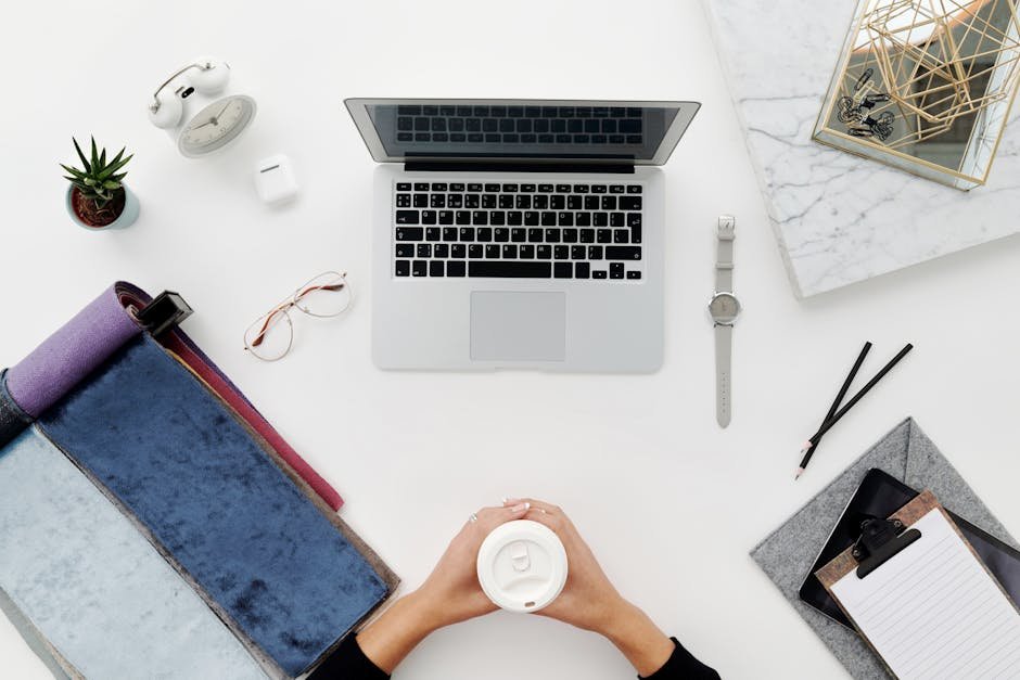 Top view of a modern desk setup with laptop, coffee cup, and office accessories in a minimalist style.