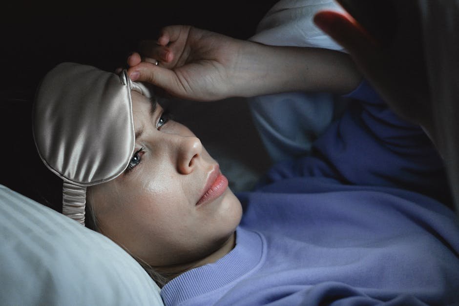A woman in bed peeking under a sleep mask to use her smartphone at night, creating a relaxing bedtime scene.